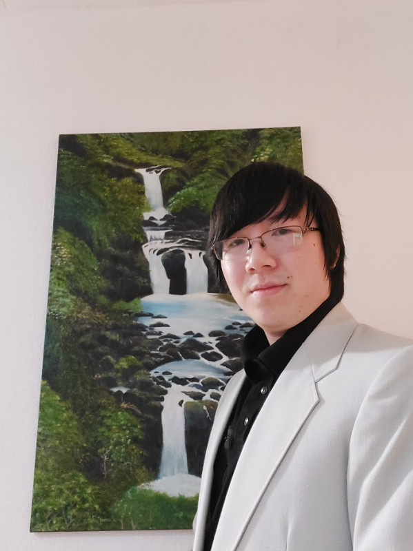 A photograph of me dressed in a white suit standing in front of a white backdrop with a canvas painting of a waterfall.