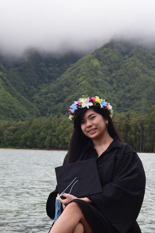 Me holding my cap while wearing my haku and gown, smiling and facing the camera. This photo was taken on the Windward side of Oahu.