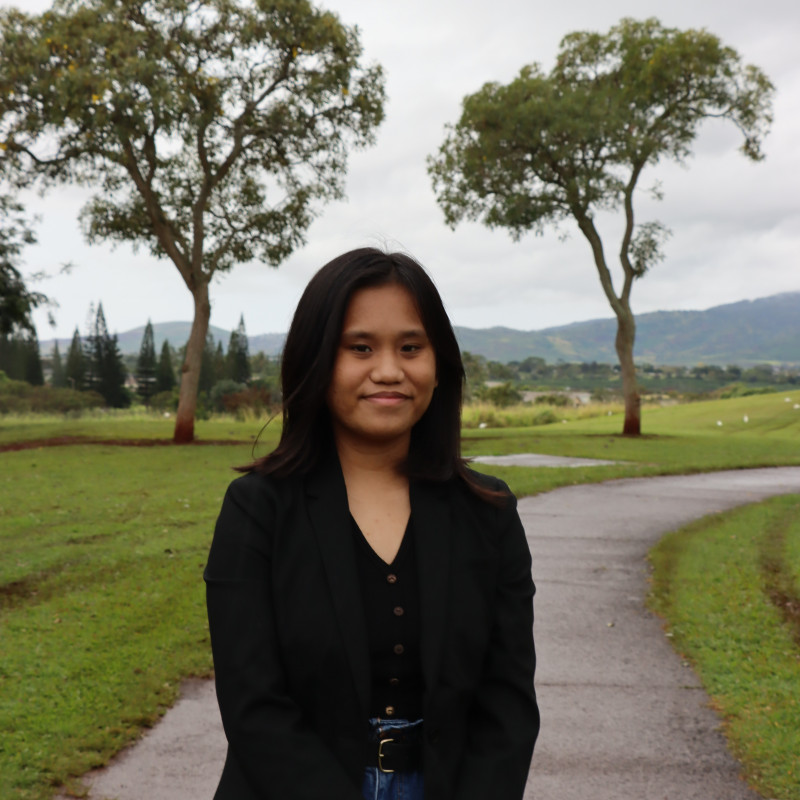 A Filipino girl with shoulder hair length wearing blue jeans and a black blazer located outside in a park.