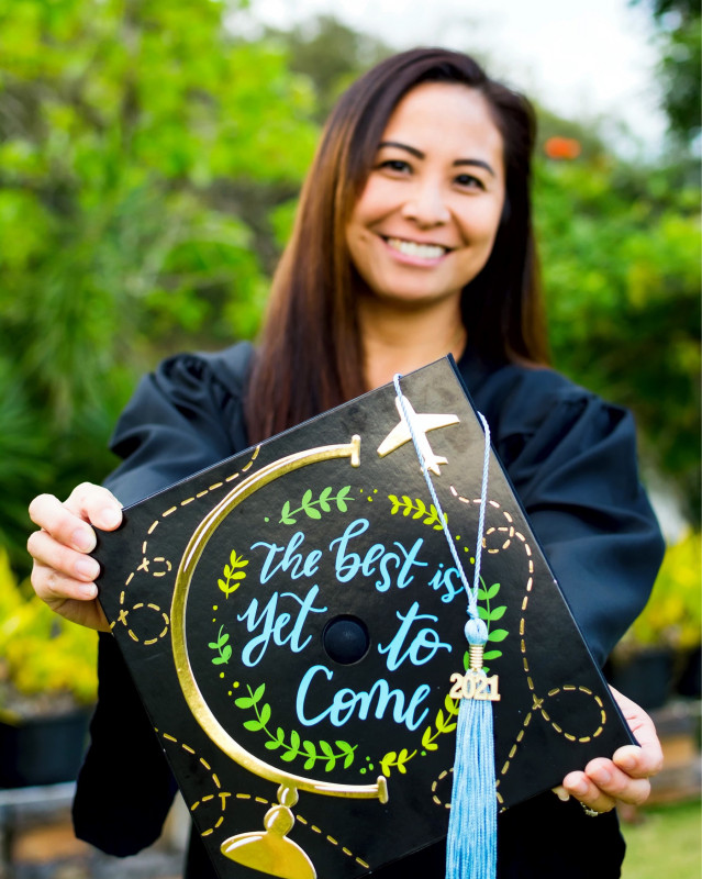 Dressed in graduation gown holding a sign stating “the best is yet to come”