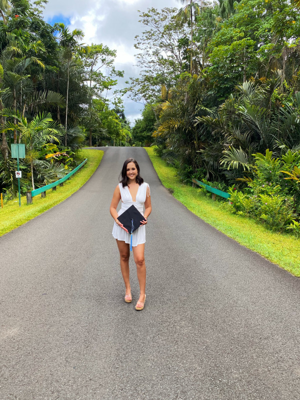 White dress standing in the middle of road holding cap and gown