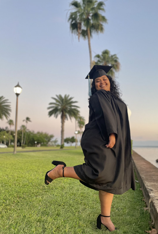 I am wearing my cap n gown while posing with one of my legs kicked up behind me.