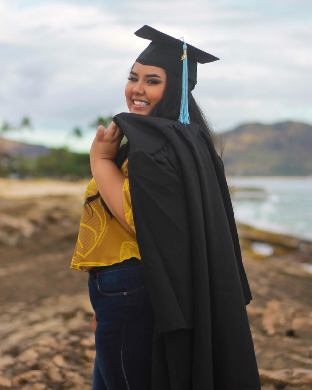 Graduate is wearing her cap and gown at a beach setting.