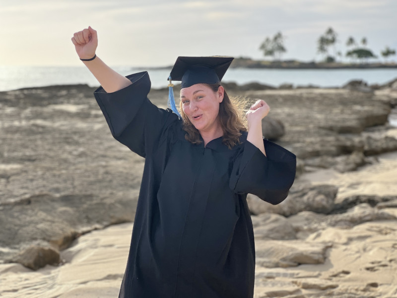 Female in graduate cap and gown cheering with arms up like "woohoo"