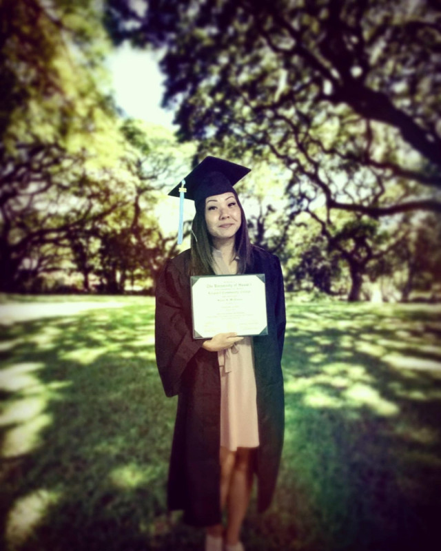 cap and gown full body portrait with diploma taken in shady outdoor area