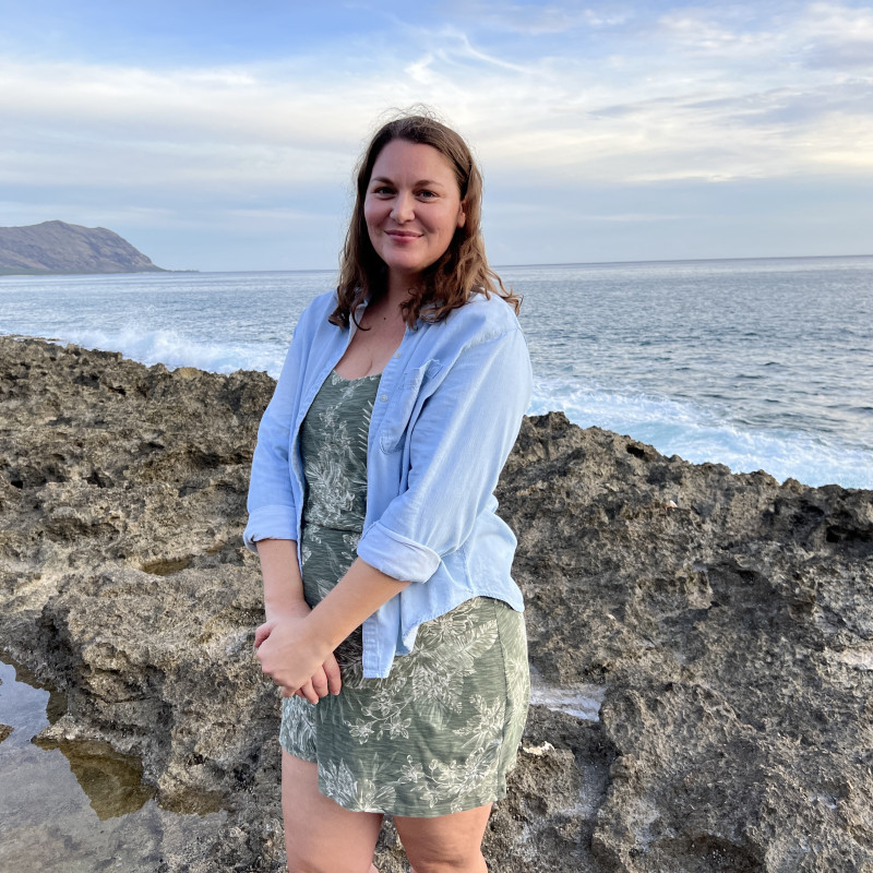 Female in green dress with baby blue overshirt, standing near the ocean