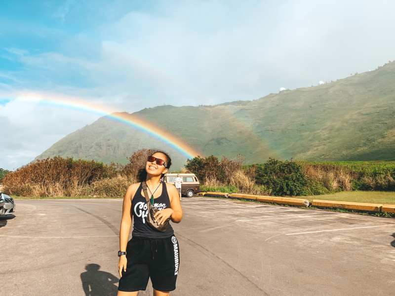 A girl with sunglasses smiling under a rainbow