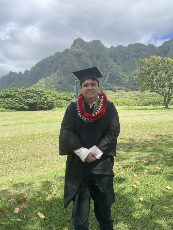 Genesis standing in graduation garb, standing in a field.