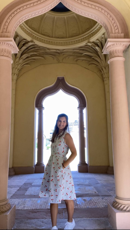 Morgan standing in an archway wearing a blue and white dress smiling.