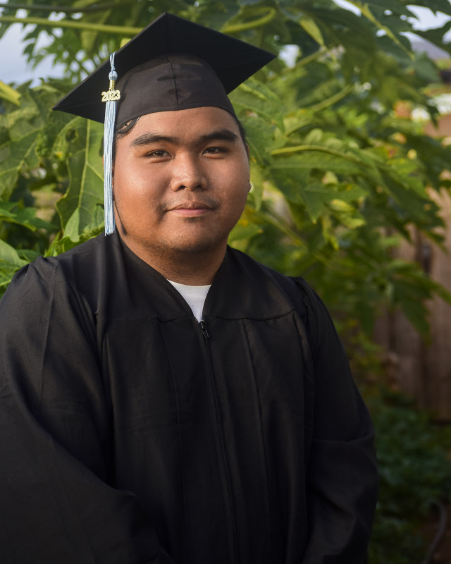 A self-portrait wearing cap and gown in front of Papaya trees.