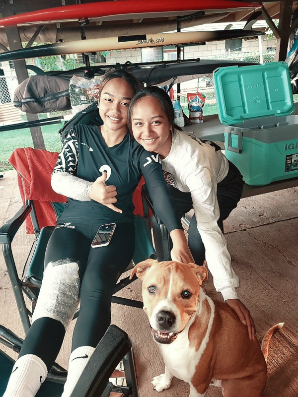 This image is a picture of my sister sitting on a chair from home(she injured her knee form playing three tournaments at the Hawaiian Convention Center).   On the right hand side, is me along with dog who is colored white and tan looking at the camera so foundily.