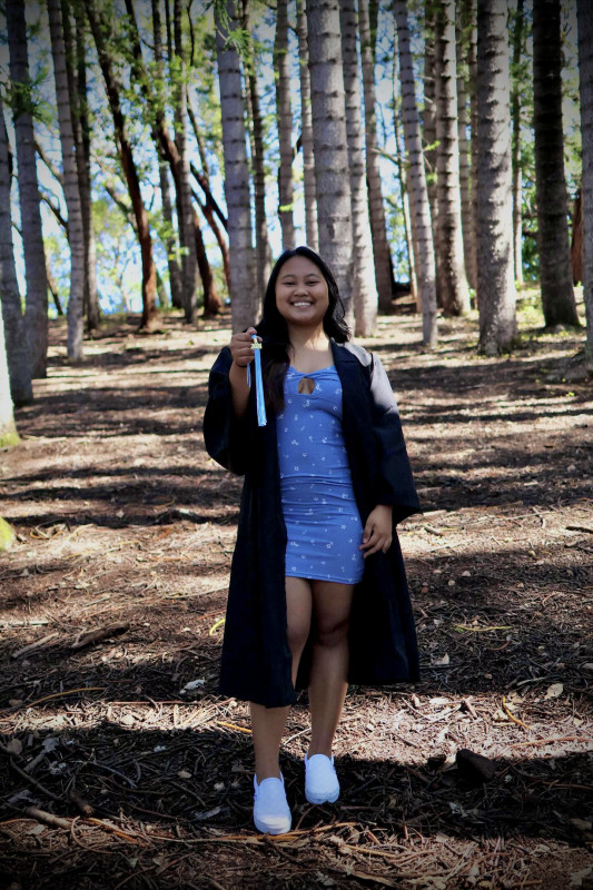 wearing black gown with blue dress inside while holding the tassel