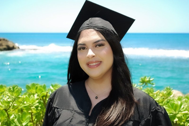 A photo of me in my cap and gown. The background is the beach
