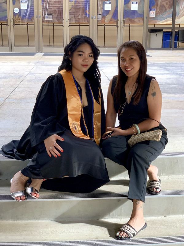 The graduate is sitting with her mom on the stairs