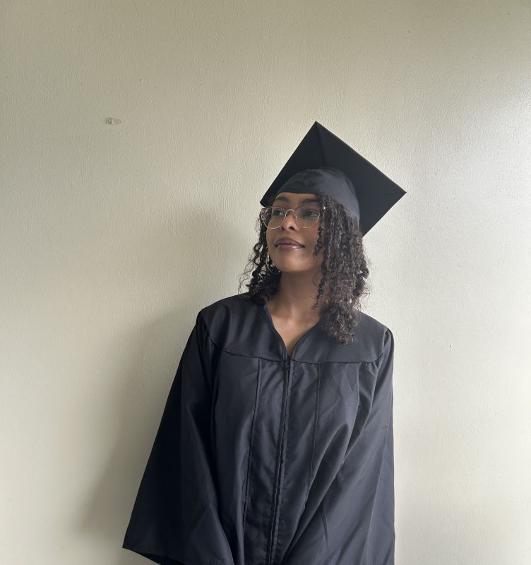 Me standing against wall in graduation gown.