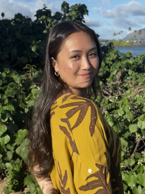 Over the shoulder smiling and standing in front of greenery.
