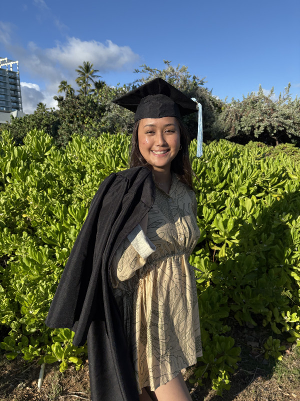 Side picture of me holding my gown over my shoulder and my cap on my head.