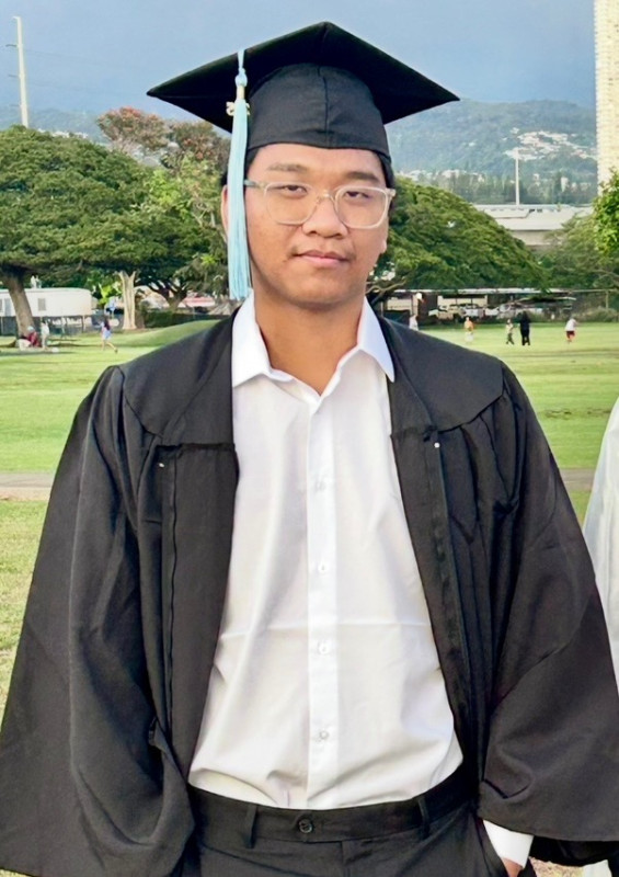 Wearing a White Long-Sleeved Collared Shirt , The cap and tassel and an opened gown, standing with his hands in his pockets on a field