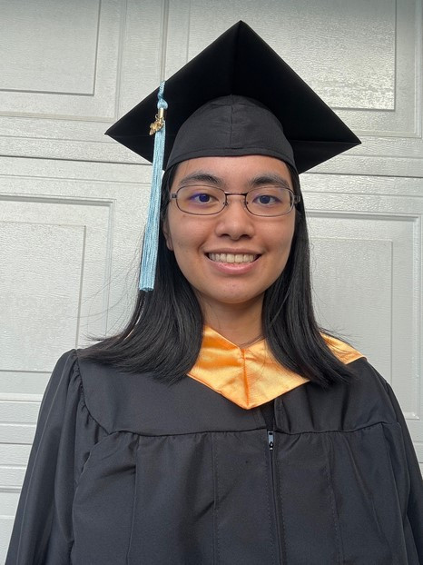 A portrait photo of myself wearing the LEE CC cap, gown, and honors hood. There is a white brick patterned background.